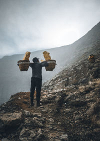 Rear view of man standing on rock against sky