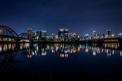 Illuminated buildings reflecting on river against sky at night