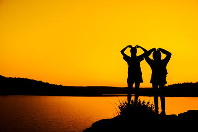 Silhouette people standing by lake against orange sky