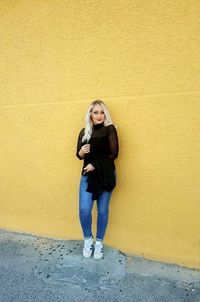 Portrait of young woman standing against yellow wall