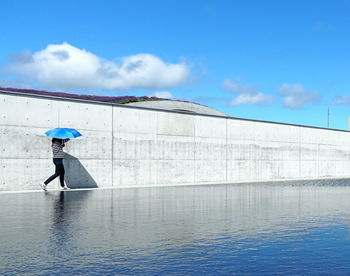 Side view of woman with umbrella against sky and water