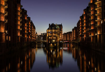 Reflection of illuminated city in water at sunset