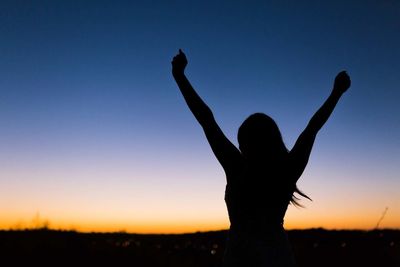 Silhouette woman with arms raised standing against blue sky during sunset