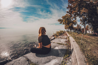 Rear view of woman sitting on shore against sky