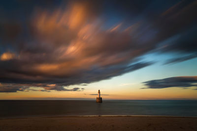 Lighthouse by sea against sky during sunset