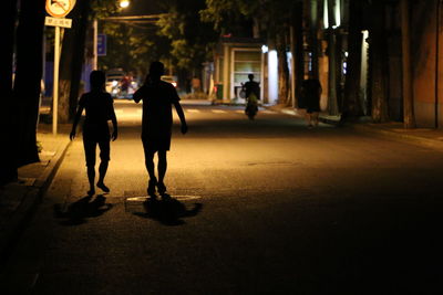 Silhouette people walking on illuminated street at night