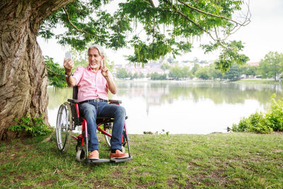 Portrait of smiling man sitting by lake against trees