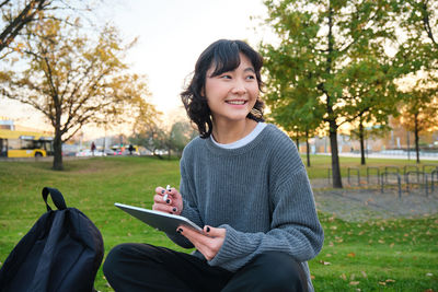 Young woman using mobile phone while sitting on field