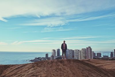 Full length of man standing on sand against sea and city