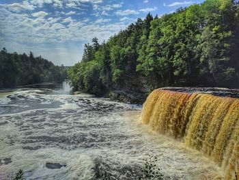 Scenic view of waterfall amidst trees against sky