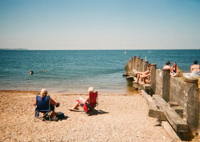 People sitting on beach by sea against sky