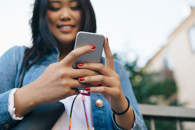 Low angle view of smiling teenage girl holding smart phone