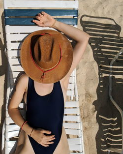 Woman in bodysuit with hat lying on chair at beach