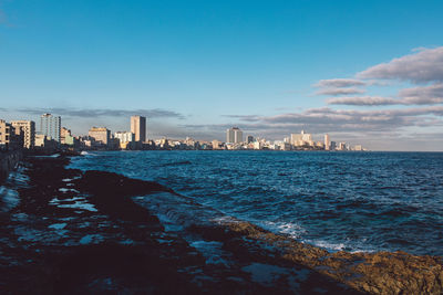 Sea by city buildings against blue sky