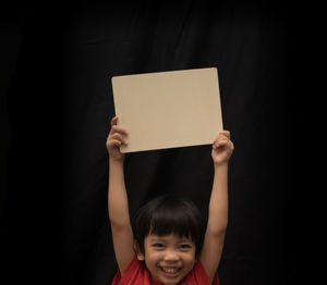 Portrait of smiling girl holding blank placard against black background