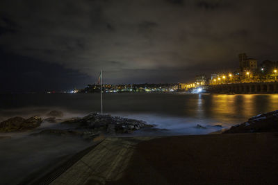 Illuminated city by sea against sky at night