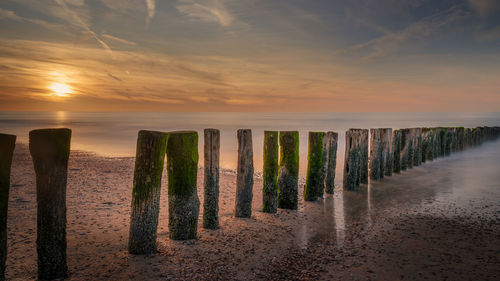 Wooden posts on beach against sky during sunset