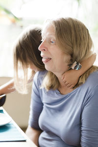 Close-up of granddaughter with arm around grandmother at home 