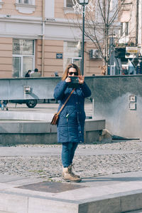 Full length of woman photographing while standing on footpath