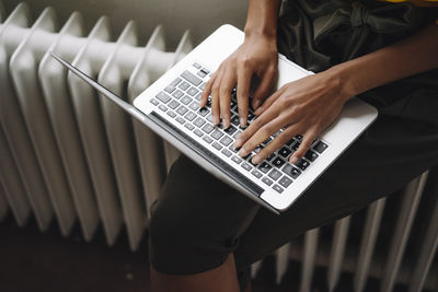 Woman sitting on heater using laptop