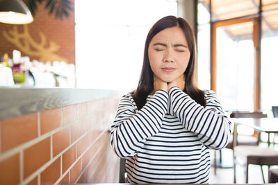 Young woman suffering from neck pain while sitting in restaurant