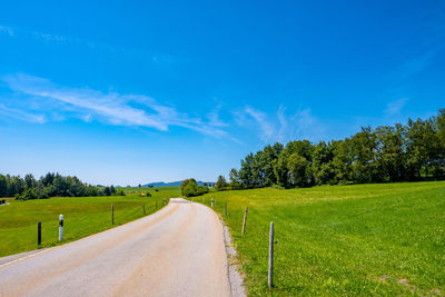 Empty road amidst field against blue sky