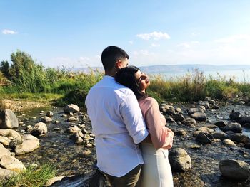 Rear view of couple embracing while standing at lakeshore