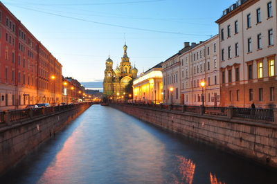 Canal amidst illuminated buildings against sky in city
