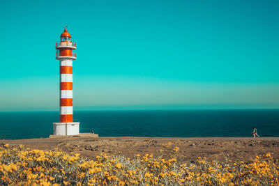 Lighthouse on beach by sea against sky