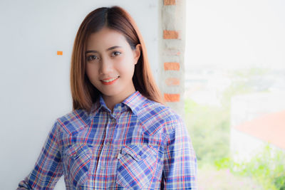 Portrait of smiling young woman standing against wall