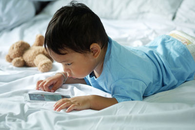 Side view of baby boy using smart phone while lying on bed