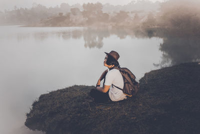 Man sitting at lakeshore during foggy weather