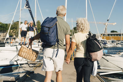 Rear view of senior couple holding hands walking on pier at harbor