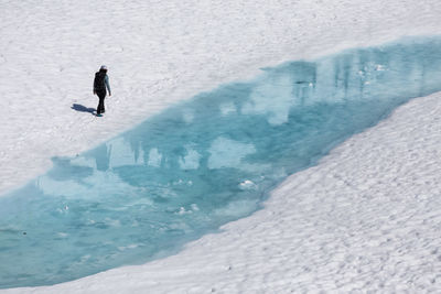 Drone view of unrecognizable female hiker walking along melting lake with clear blue water during vacation in british columbia