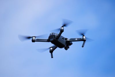 Low angle view of drone flying against blue sky