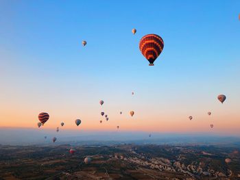 Hot air balloons flying over landscape against sky during sunset