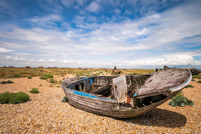 Abandoned boat moored on shore against sky