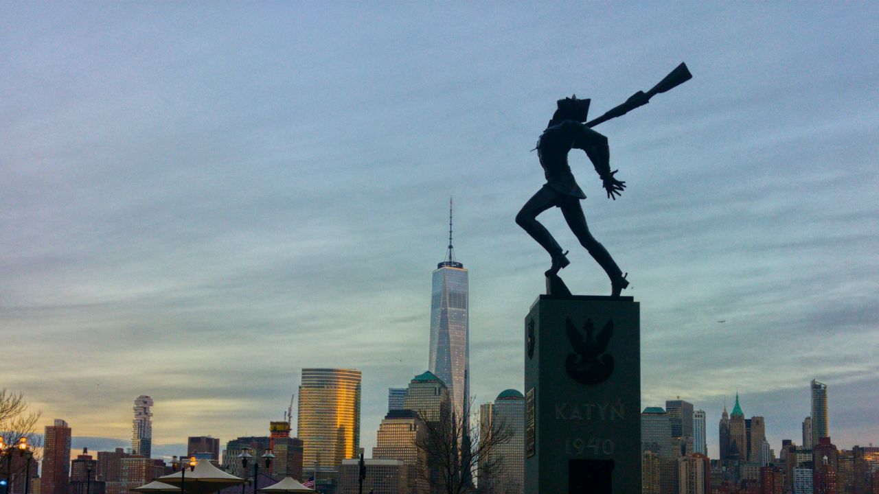 LOW ANGLE VIEW OF STATUE WITH CITY IN BACKGROUND
