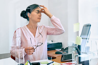 Tired and stressed business woman touching her head with hand, sitting in office at desk