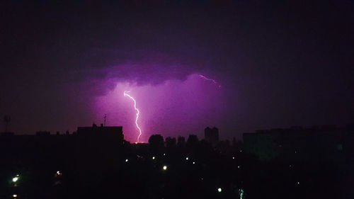 Lightning over silhouette cityscape against sky at night