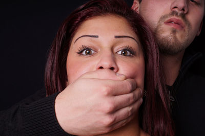 Young man covering woman mouth with hand against black background
