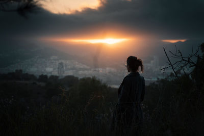 Rear view of woman standing on land against sky during sunset