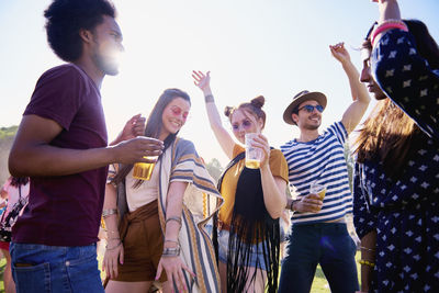 Friends holding drinks in glasses while dancing against sky