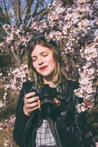 Portrait of beautiful young woman standing by flower tree