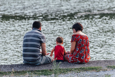 Rear view of family sitting by lake