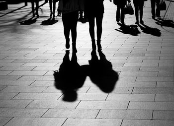 Low section of silhouette people walking on street during sunny day