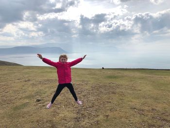 Full length of girl jumping on field against sky