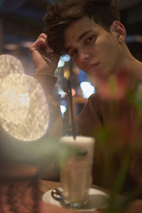 Portrait of young man sitting with drink in cafe at night