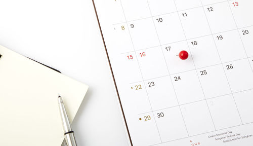 Close-up of diary with pen and thumbtack pinned calendar on table