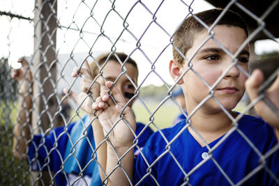 Boy looking through fence while standing in dugout